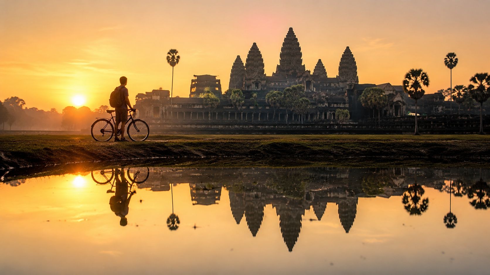A traveler with a bicycle watching the sunrise over the ancient Angkor Wat temple in Cambodia.